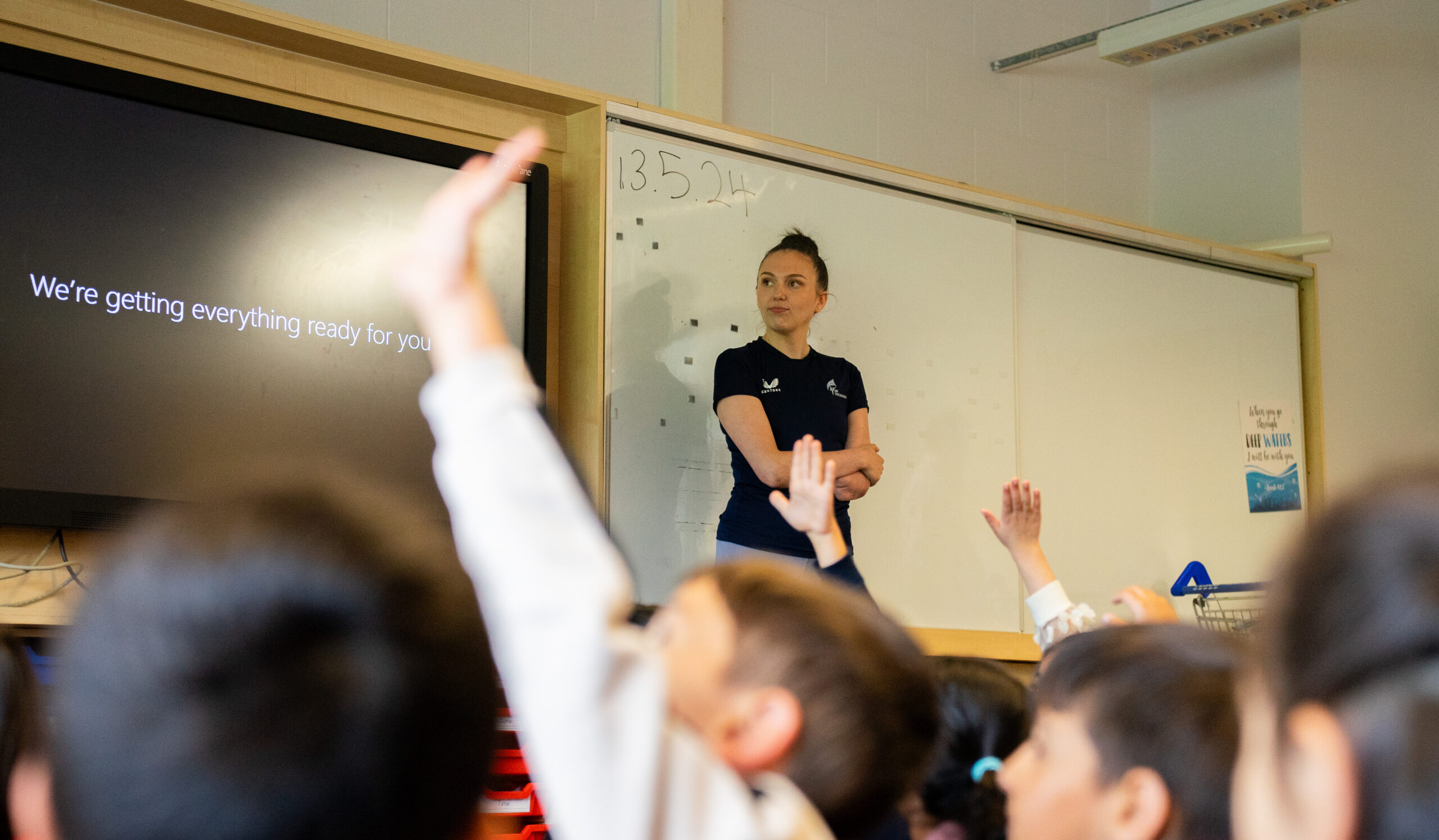 A brown haired woman stood in front of a classroom of children.